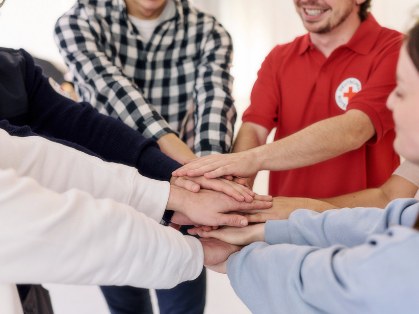 Eine Gruppe Menschen steht im Kreis und legt als Team die Hände übereinander